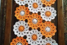 Caminho de mesa em crochê com flores em tons de laranja e branco.