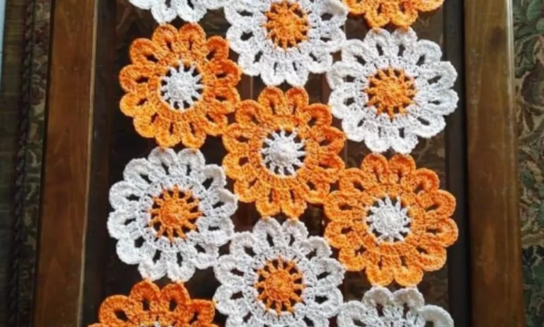 Caminho de mesa em crochê com flores em tons de laranja e branco.