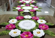 Caminho de mesa de crochê com flores coloridas em tons de rosa e branco, com detalhes verdes, em uma mesa.