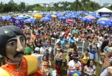 Multidão comemorando o Carnaval ao ar livre com boneco gigante e guarda-sóis coloridos.