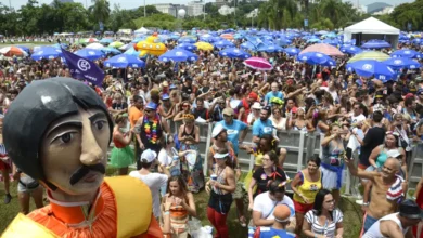 Multidão comemorando o Carnaval ao ar livre com boneco gigante e guarda-sóis coloridos.