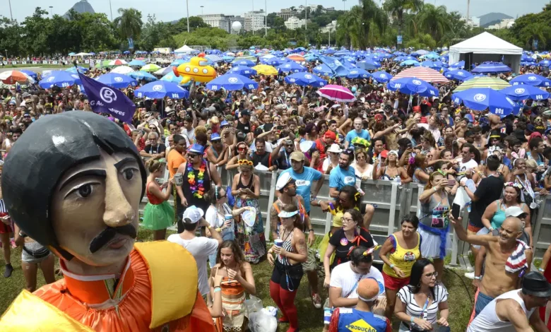 Multidão comemorando o Carnaval ao ar livre com boneco gigante e guarda-sóis coloridos.