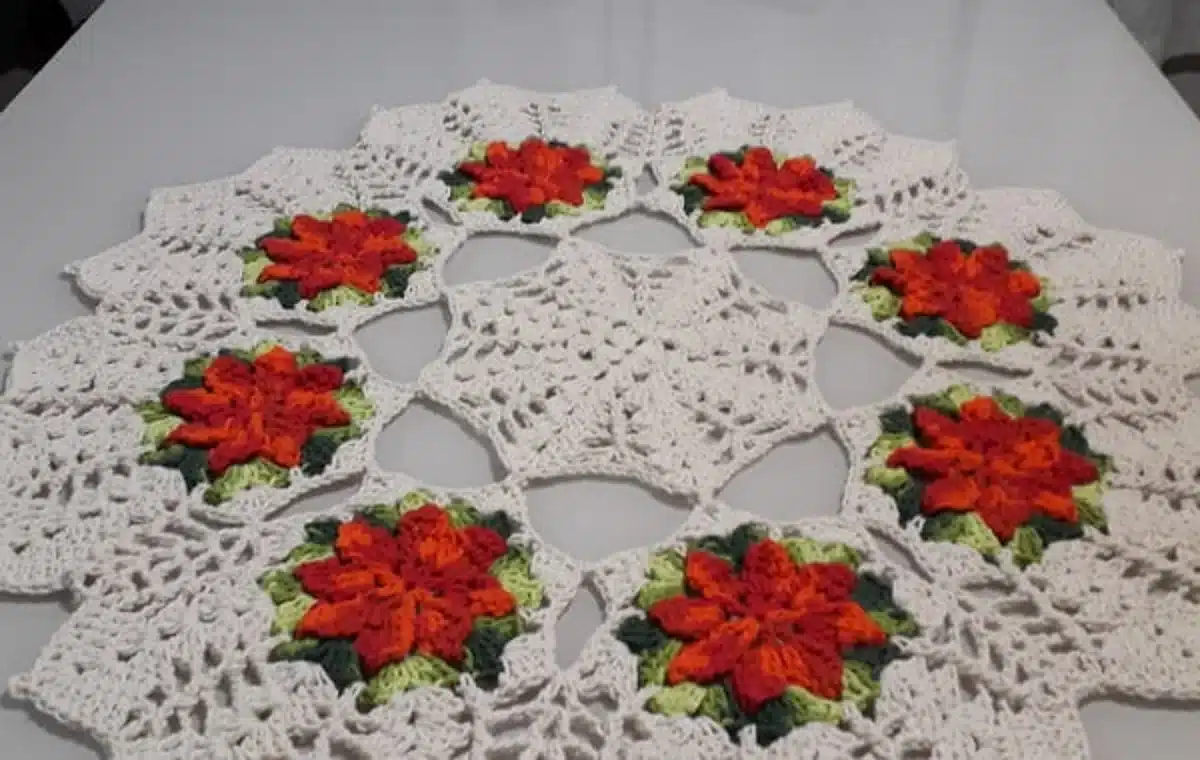 Centro de mesa de crochê com flores coloridas, mostrando um design bonito e elegante em tons de branco, laranja, verde e vermelho.
