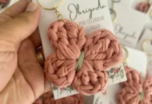 Chaveiro de crochê em forma de borboleta rosa, com detalhes em verde, preso a uma chaveiro dourado.