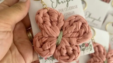 Chaveiro de crochê em forma de borboleta rosa, com detalhes em verde, preso a uma chaveiro dourado.
