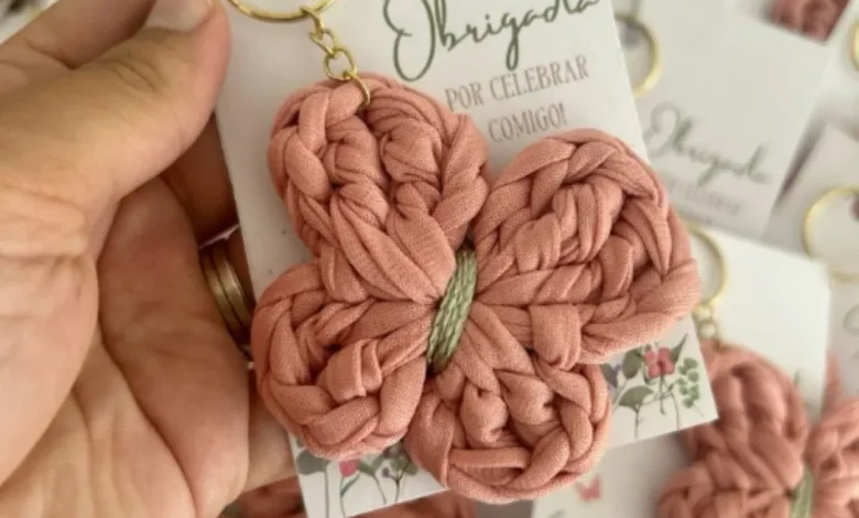 Chaveiro de crochê em forma de borboleta rosa, com detalhes em verde, preso a uma chaveiro dourado.