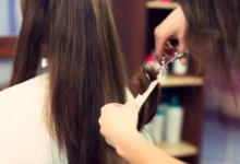 Cabeleireiro cortando cabelo longo castanho com tesoura e pente em salão de beleza.