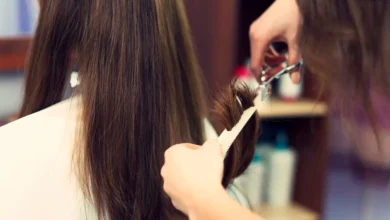 Cabeleireiro cortando cabelo longo castanho com tesoura e pente em salão de beleza.