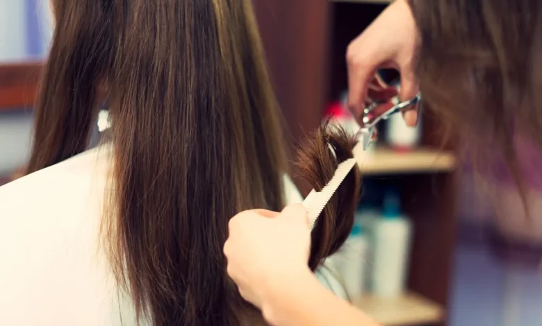 Cabeleireiro cortando cabelo longo castanho com tesoura e pente em salão de beleza.