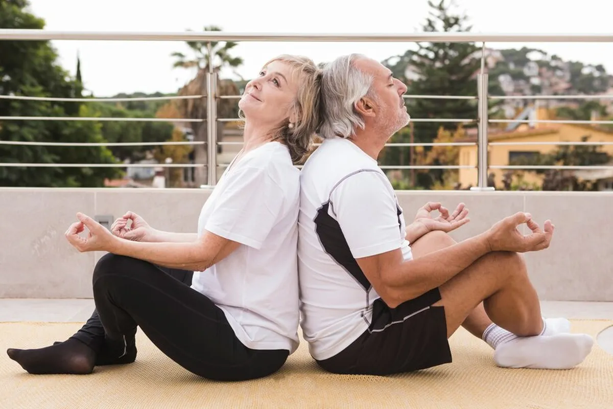 Casal maduro praticando meditação ao ar livre em uma posição relaxante.