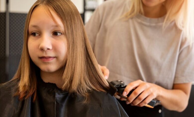 Criança recebendo um corte de cabelo no salão, com o cabelo liso sendo aparado por um profissional.