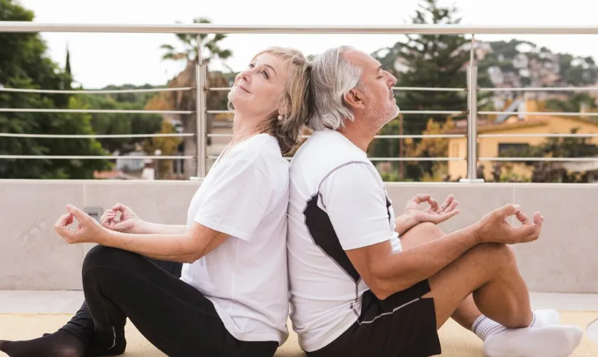 Casal de idosos praticando meditação ao ar livre, promovendo o bem-estar físico e mental.