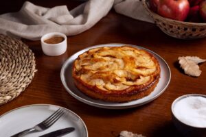 Bolo de maçã e canela servido em prato rústico com ingredientes ao lado.