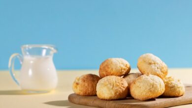 Pãozinhos de leite em pó fresquinhos, em uma tábua de madeira, acompanhados de uma jarra de leite.