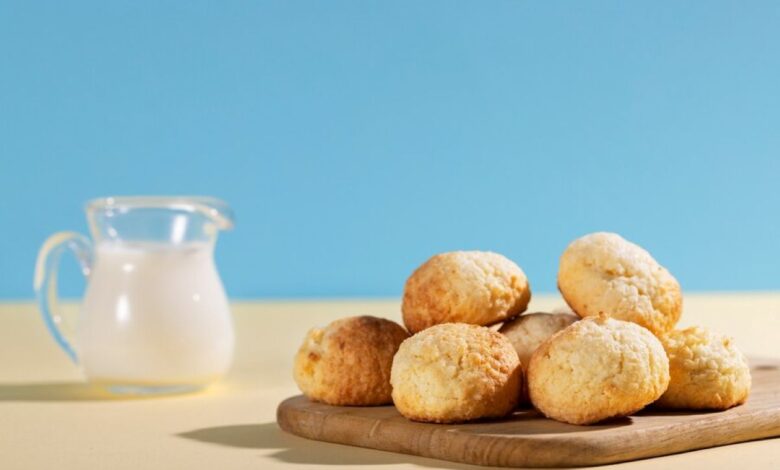 Pãozinhos de leite em pó fresquinhos, em uma tábua de madeira, acompanhados de uma jarra de leite.