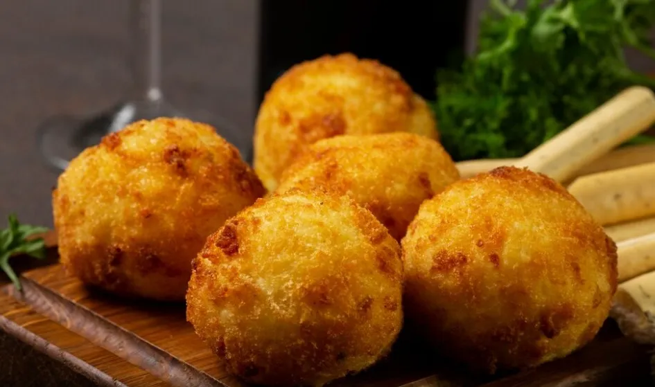 Bolinhos de queijo sem trigo crocantes e dourados, servidos em tábua rústica.