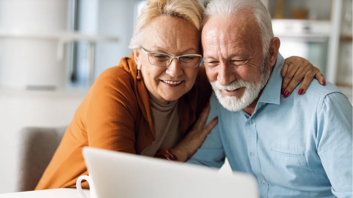 Casal idoso sorrindo enquanto utiliza o computador.