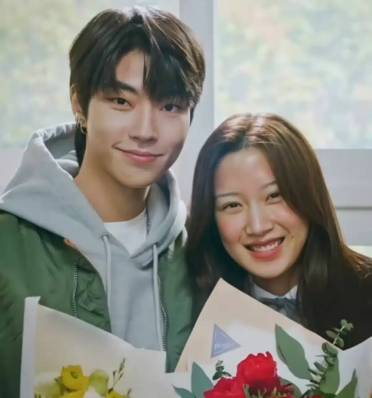 Casal sorrindo enquanto segura buquês de flores, em uma cena romântica de dorama.