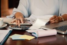 Pessoa revisando documentos e calculando dívidas em uma mesa de escritório, representando o processo de gestão financeira após a morte de um titular.