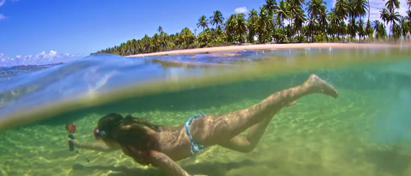 Mulher mergulhando em uma piscina natural na Península de Maraú, cercada por águas cristalinas e coqueirais