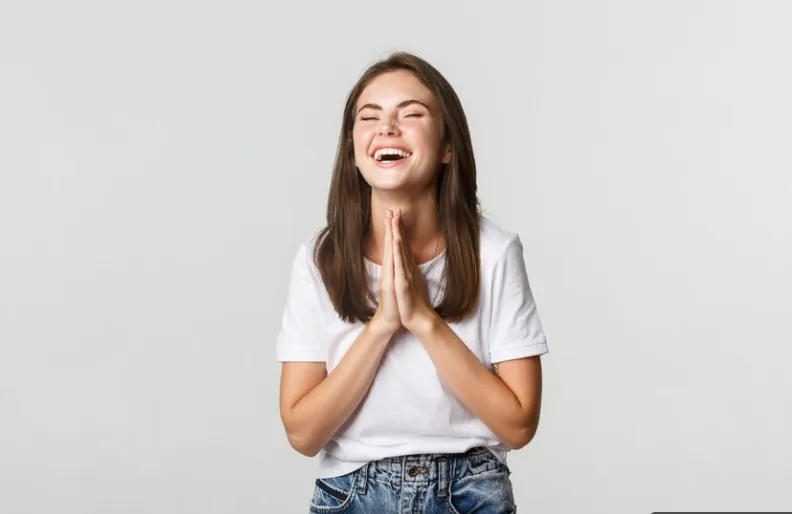 Mulher sorridente expressando gratidão com as mãos unidas em sinal de agradecimento.