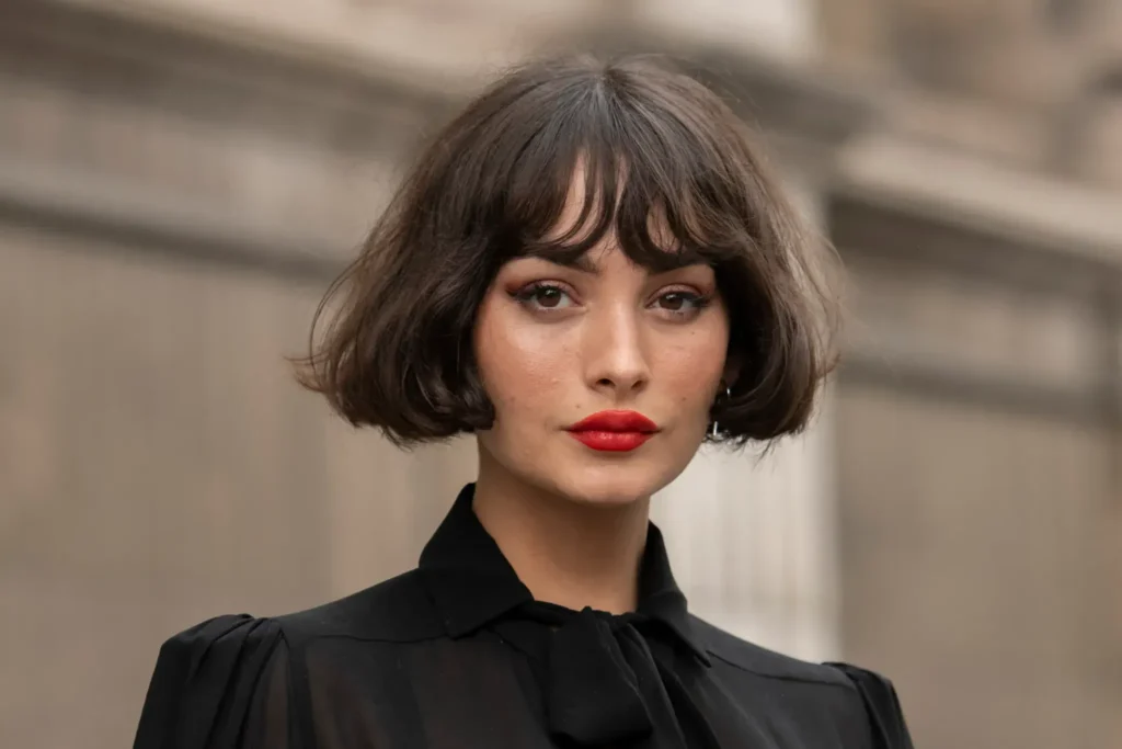 Mulher com corte French Bob, cabelo curto e franja suave, vestindo blusa preta e batom vermelho