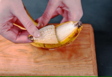 Mãos abrindo uma banana madura sobre uma tábua de madeira.