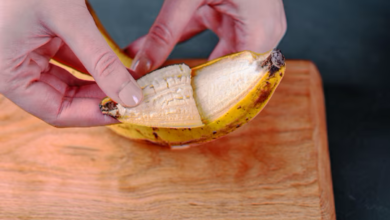 Mãos abrindo uma banana madura sobre uma tábua de madeira.