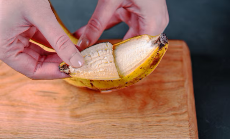 Mãos abrindo uma banana madura sobre uma tábua de madeira.