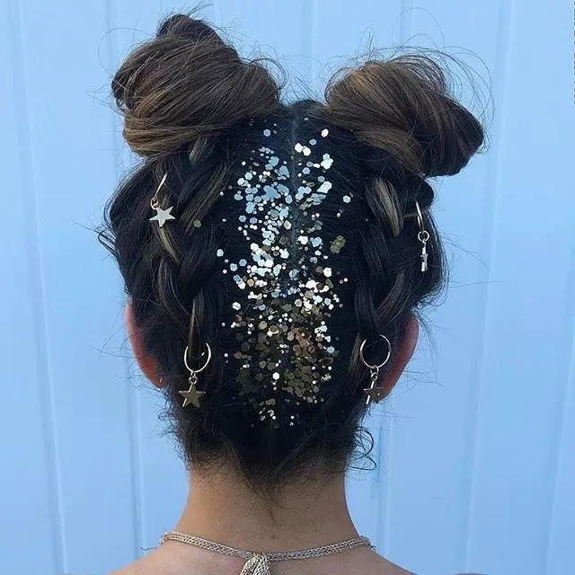 Penteado com tranças e coque duplo, decorado com glitter na raiz e acessórios metálicos.