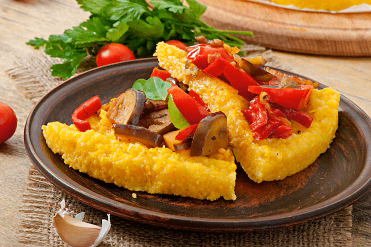 Fatias de bolo de milho salgado recheado com legumes grelhados, servidas em um prato rústico.