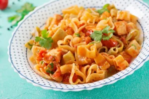  Prato de macarrão ao alho e óleo com pedaços de frango e tomate, servido com ervas frescas.