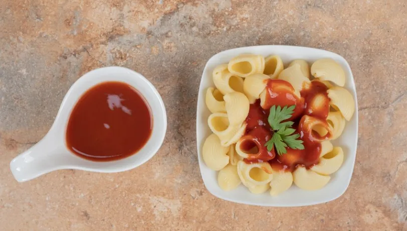 Prato de macarrão com molho de tomate e ervas frescas ao lado de uma porção extra de molho.