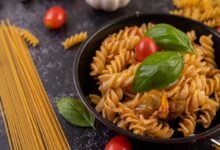 Prato de macarrão fusilli ao alho e óleo, decorado com tomate cereja e folhas de manjericão.