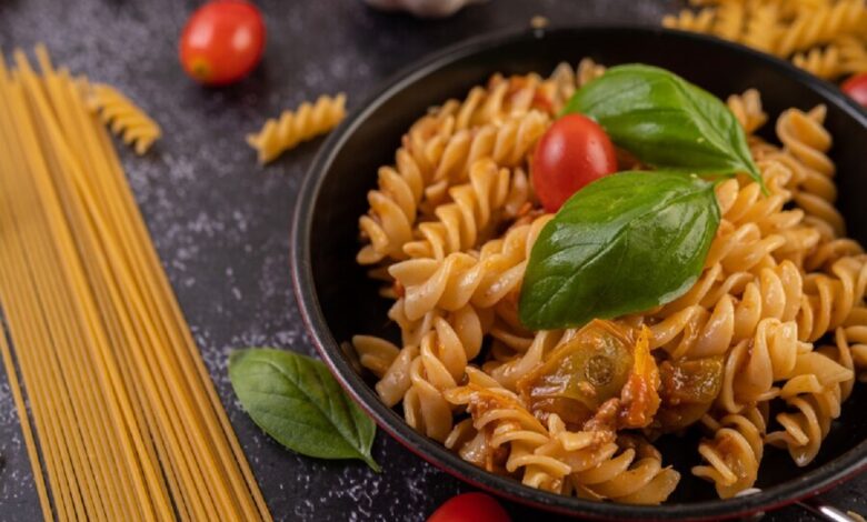 Prato de macarrão fusilli ao alho e óleo, decorado com tomate cereja e folhas de manjericão.