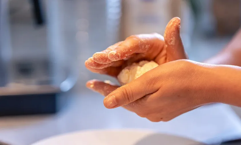 Pessoa modelando a massa de biscoito de polvilho com as mãos enfarinhadas.