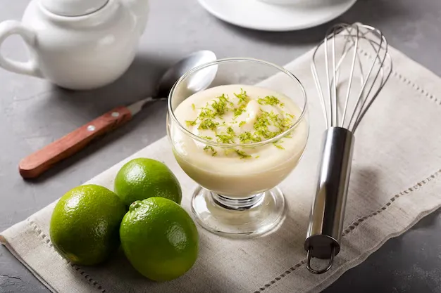 Mousse de limão cremoso servido em uma taça, decorado com raspas de limão e acompanhado de limões frescos.