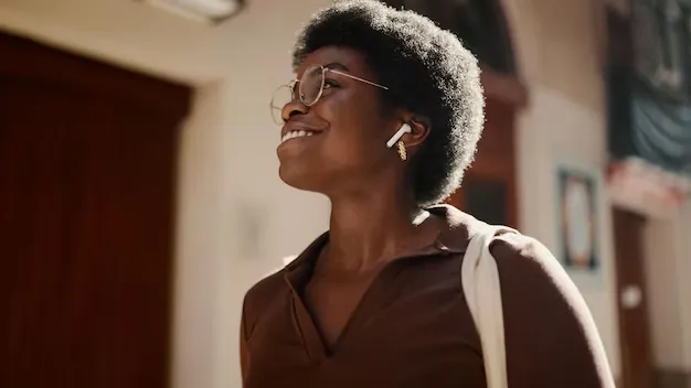 Mulher com cabelo afro sorrindo ao ar livre, usando óculos, fones de ouvido e bolsa de tecido.