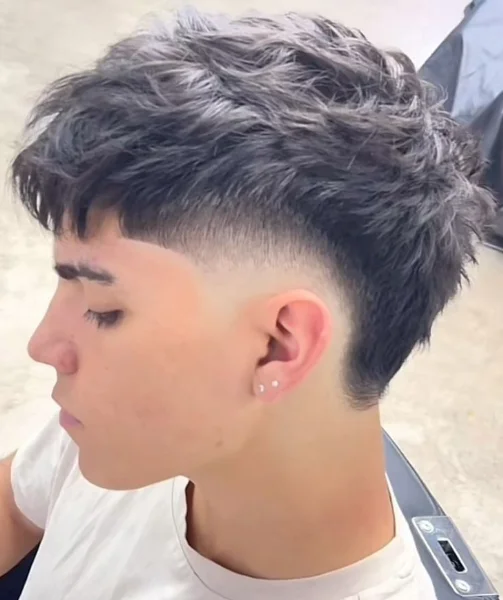 Corte de cabelo moderno estilo mullet com fade nas laterais e fios bagunçados na parte superior.