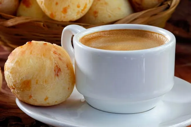 Pão de queijo recém-assado ao lado de uma xícara de café, compondo uma cena de café da manhã acolhedora.