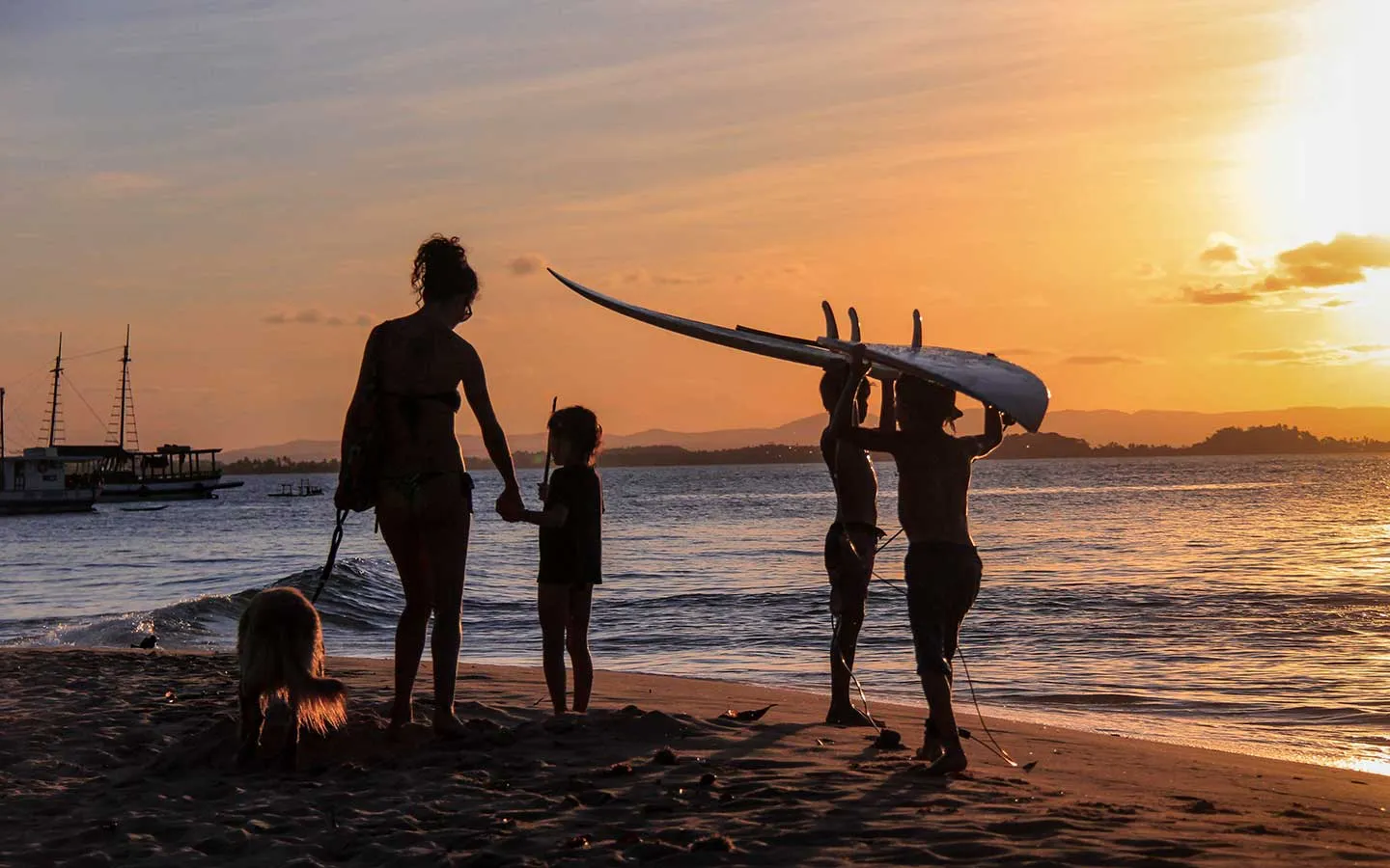 Silhuetas de pessoas e um cachorro na praia durante o pôr do sol na Ponta do Mutá, Península de Maraú