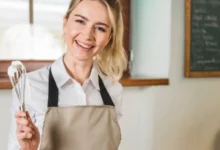 Chef sorridente segurando um fouet com creme, pronta para preparar uma sobremesa deliciosa.