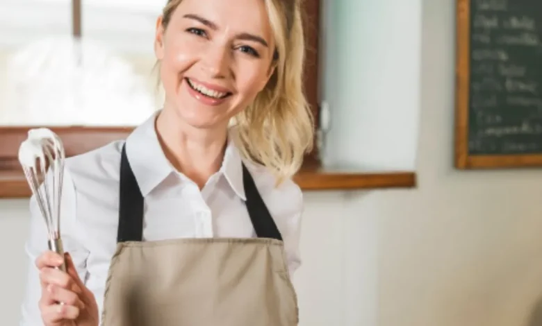 Chef sorridente segurando um fouet com creme, pronta para preparar uma sobremesa deliciosa.