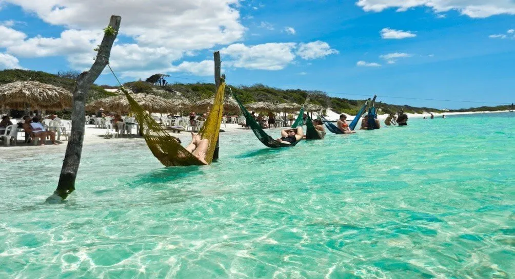 Pessoas relaxando em redes dentro do mar cristalino de Jericoacoara, um destino paradisíaco no Brasil