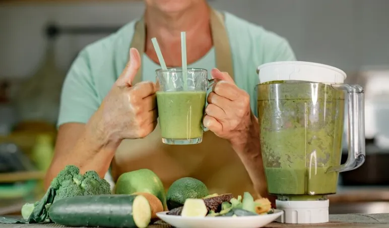 Pessoa segurando um copo de suco verde feito com ingredientes naturais e antioxidantes.