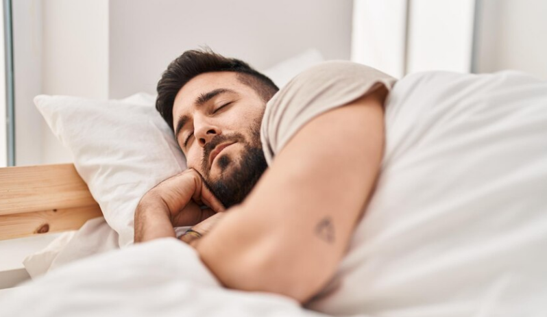 Homem de barba dormindo tranquilamente em uma cama confortável.