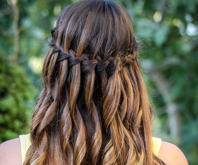 Cabelo castanho com mechas douradas em trança cascata, estilo romântico.