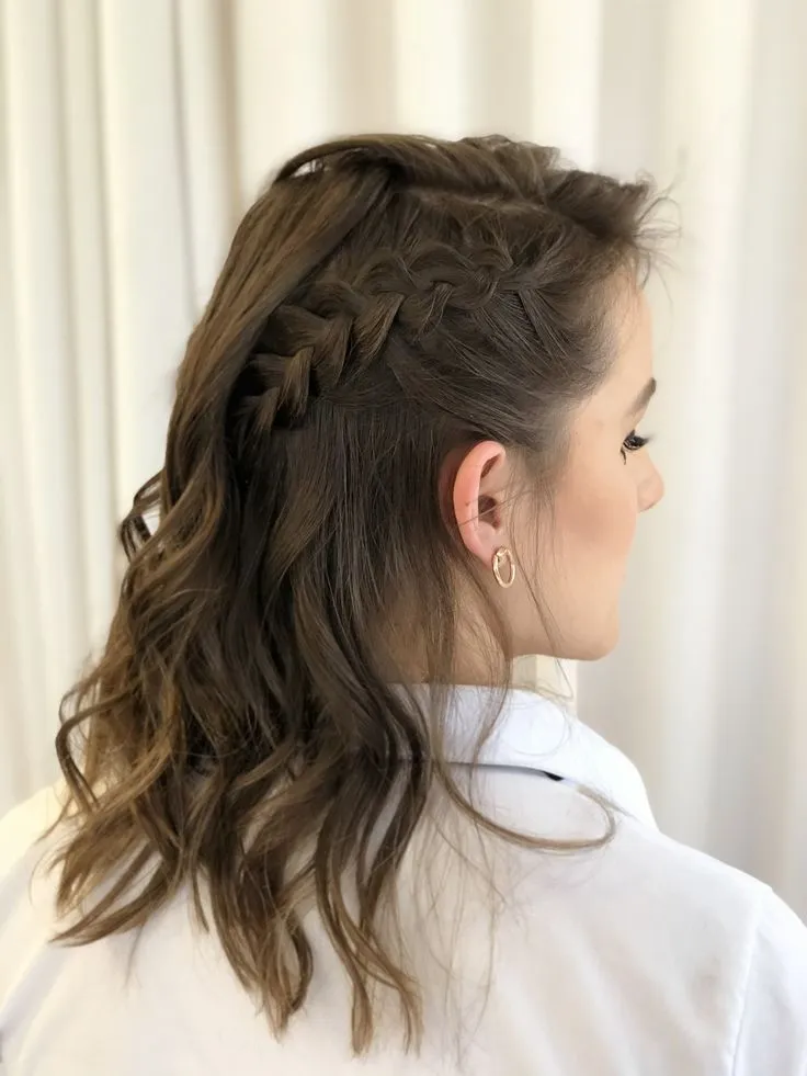  Penteado com trança lateral e cabelos ondulados soltos, criando um visual elegante e romântico.