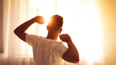 Homem espreguiçando-se pela manhã diante de uma janela iluminada pelo sol.