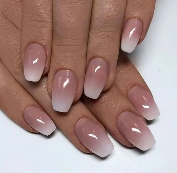 Unhas degradê em tons neutros, com transição suave do rosa claro para o branco, criando um efeito elegante e delicado